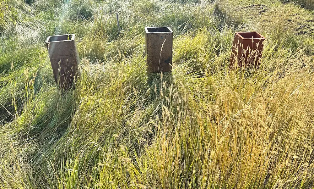 Three square clay chimney flue tiles standing upright in tall grass after an old fireplace flue was taken apart