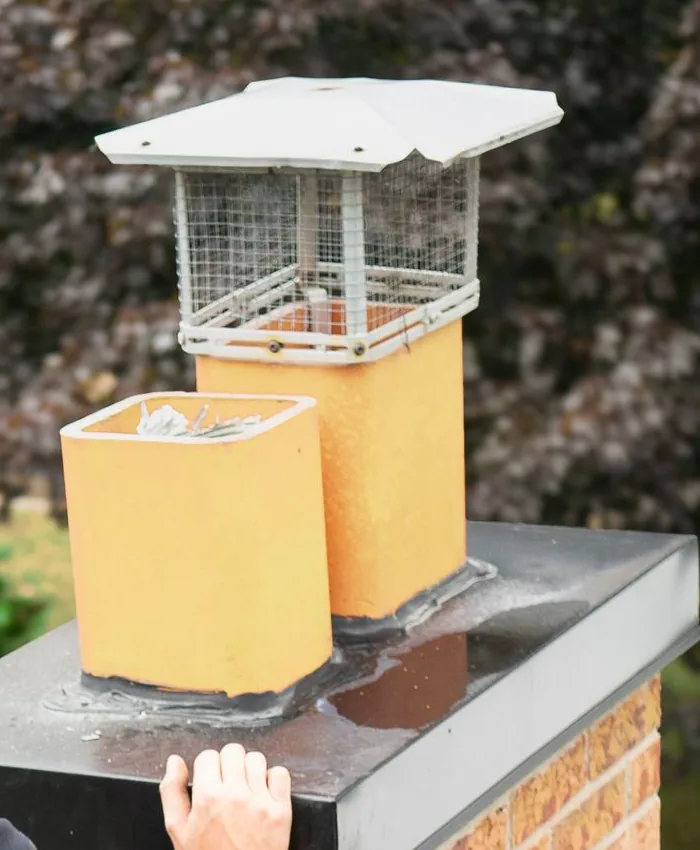 The top of a brick chimney with two square clay flue tiles sticking up through the crown, one of them covered by a wire-mesh chimney cap