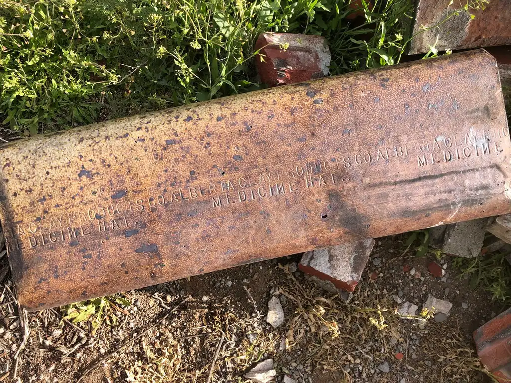 A section of old clay flue tile with stamped lettering lying in the grass among broken bricks after a chimney was taken down