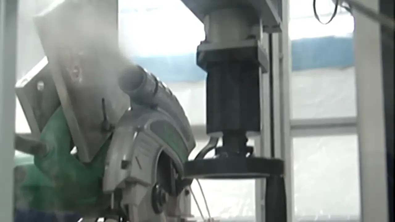 A circular saw with a dust collection hose attached cutting a fiber cement board on a test rig, with a small cloud of dust at the blade