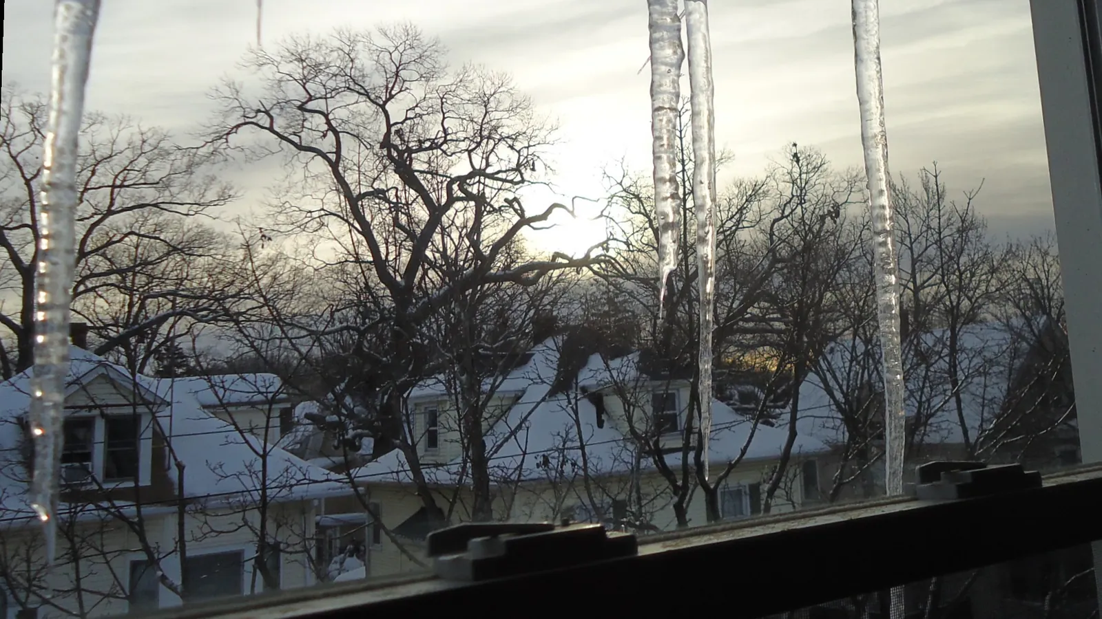 Long icicles hanging from a house gutter in front of snow-covered roofs on a winter afternoon