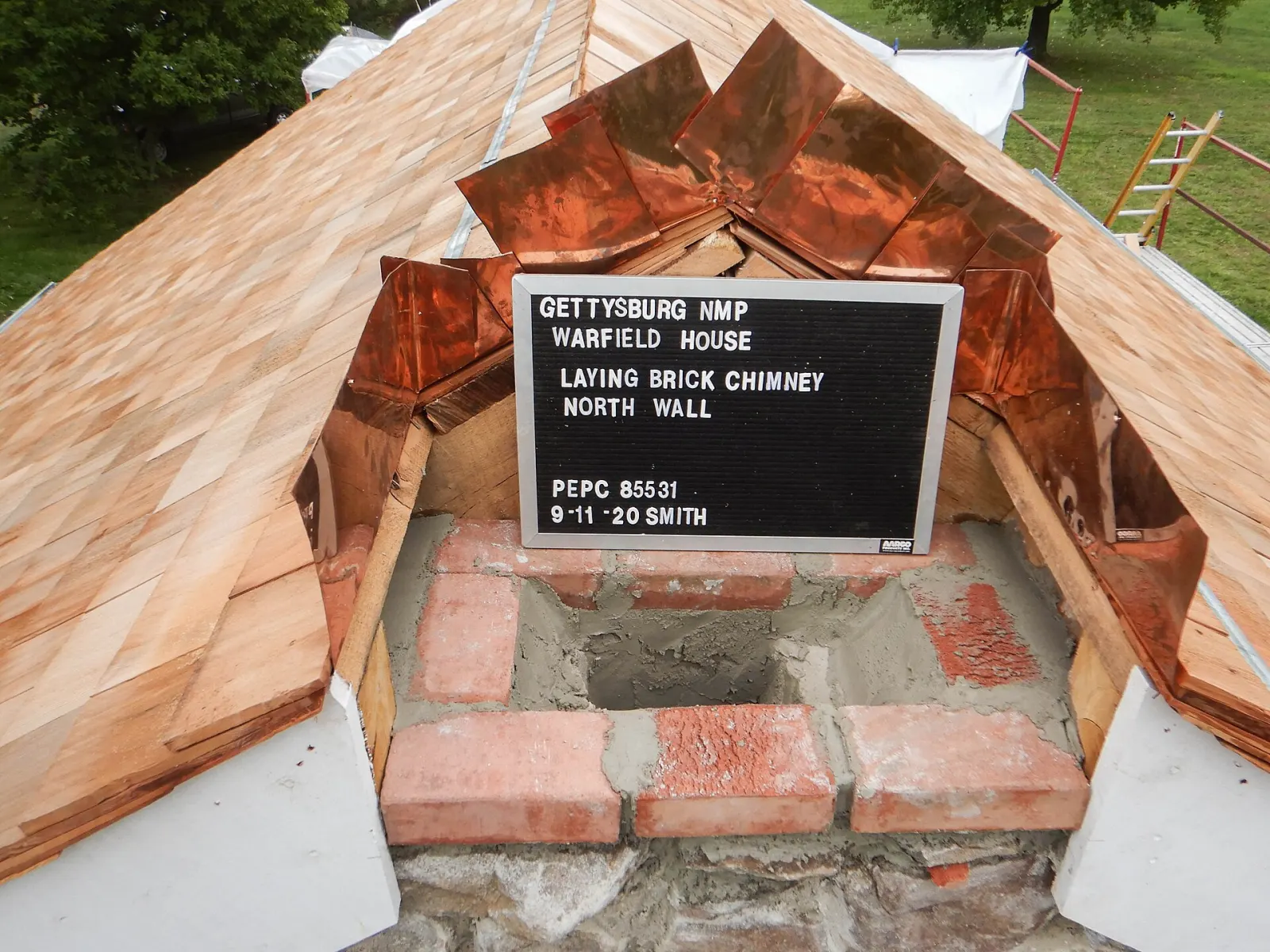 Looking down on a new brick chimney being laid through a cedar shingle roof, with copper flashing folded up around the opening