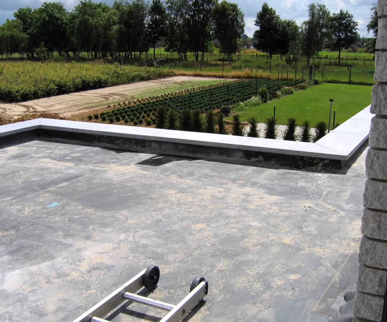 A new black EPDM membrane covering a flat roof and turned up the low parapet wall under metal coping, with a ladder resting on the roof