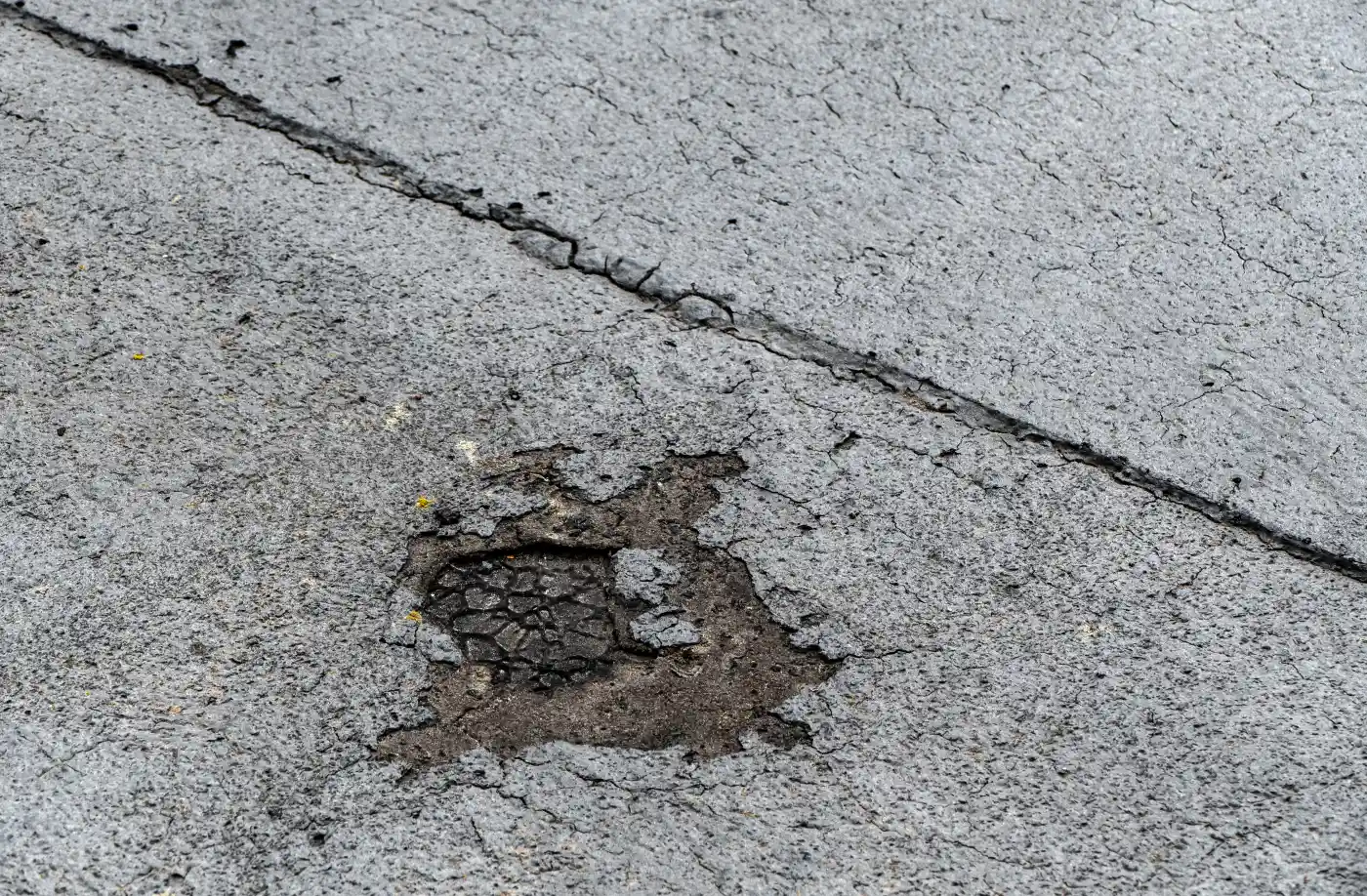 Close-up of a weathered bitumen roof surface with a worn patch exposing the layer below, next to a cracked seam